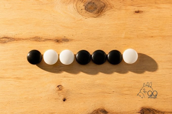 浅色松木桌面上七颗黑白围棋子一字排开，黑白随机交错